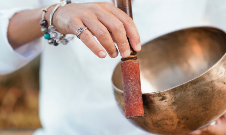 a brass coloured sound bowl with a woman's hand circling the bowl