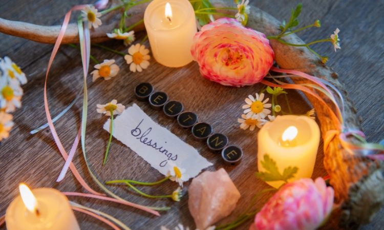 a wooden tray with blessings written on a piece of paper, candles, flowers and crystals and beltane spelled out in letters on metal buttons